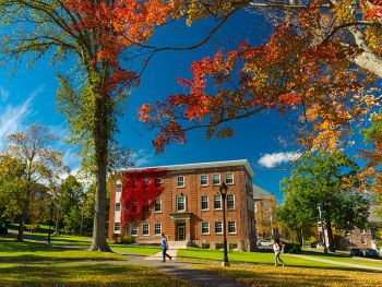 Students walk by Acadia's Rhodes Hall during the autumn. The building is bordered by trees with vibrant fall leaves.